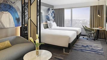 Une chambre d’hôtel avec un lit, un canapé, une petite table avec un vase et une vue sur la ville.
