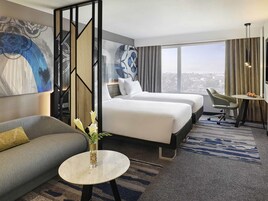 Une chambre d’hôtel avec un lit, un canapé, une petite table avec un vase et une vue sur la ville.
