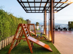 A rooftop terrace with a wooden swing set, a glass-enclosed area, and a view of the cityscape. - Novotel Suites Yogyakarta Malioboro (Yogyakarta)