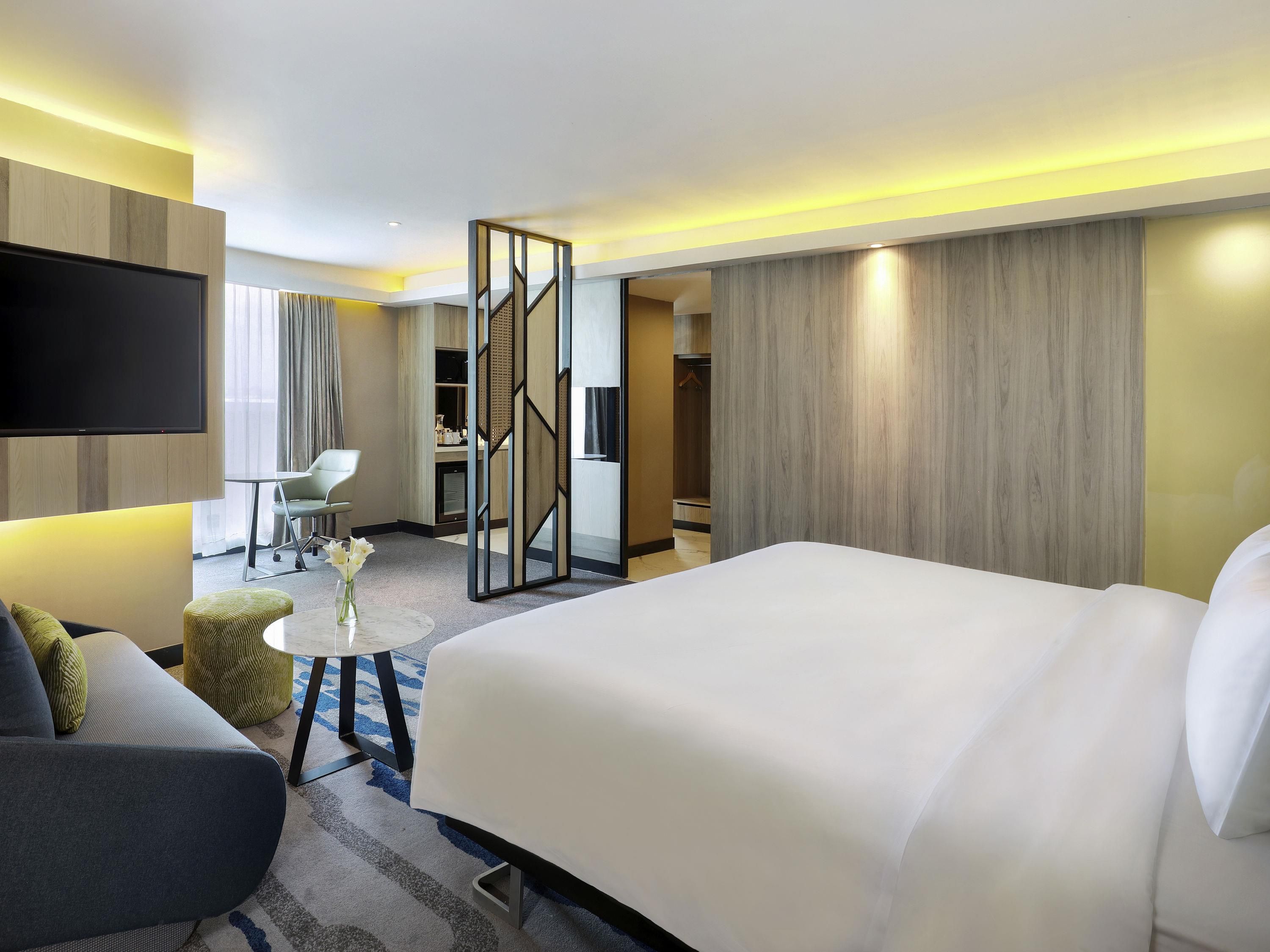 Quarto de hotel com uma cama grande, televisão, escrivaninha e uma cadeira.