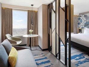 Une chambre d’hôtel avec un lit, une table ronde, une chaise, un canapé et une vue sur la ville.