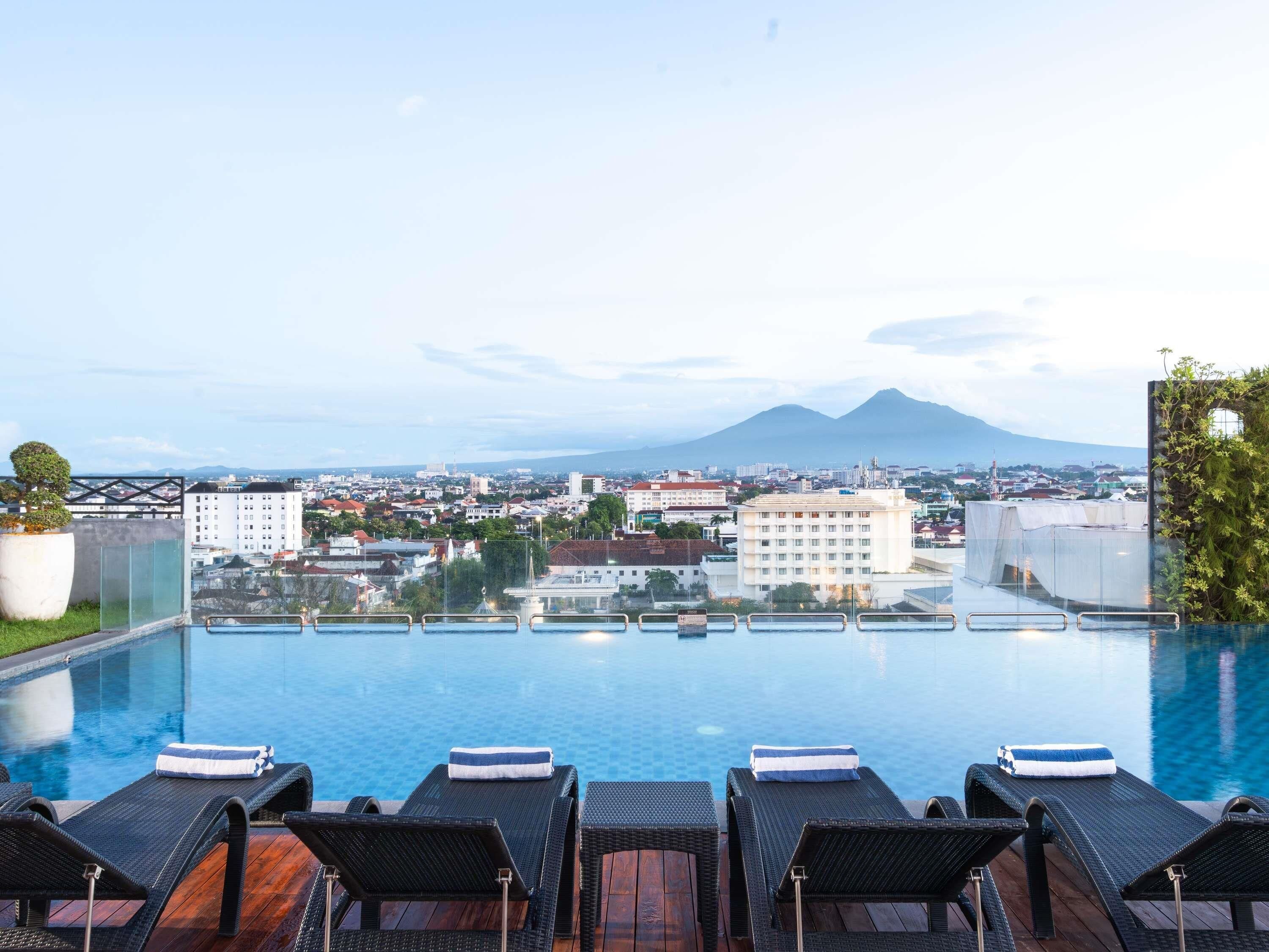 Ein Infinity-Pool mit Liegestühlen, Blick auf eine Stadtlandschaft und ein Berg in der Ferne.