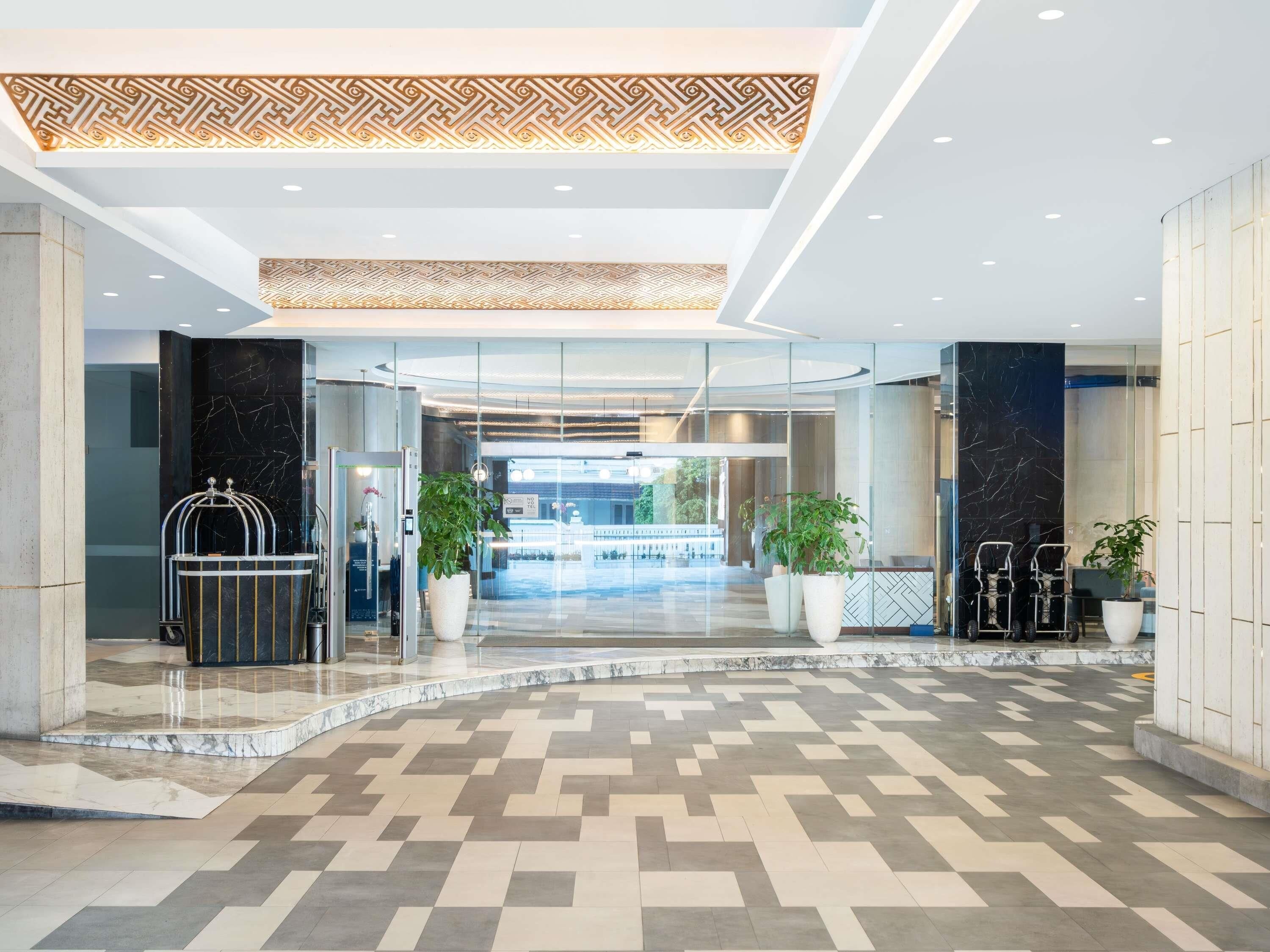 A modern hotel lobby with a geometric patterned floor, a reception desk, and potted plants.