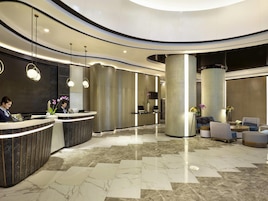 Un hall d’hôtel moderne avec un comptoir d’accueil, un espace salon et de grandes colonnes.