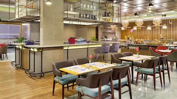 A modern restaurant with a bar area, seating with tables and chairs, and a patterned wall design.