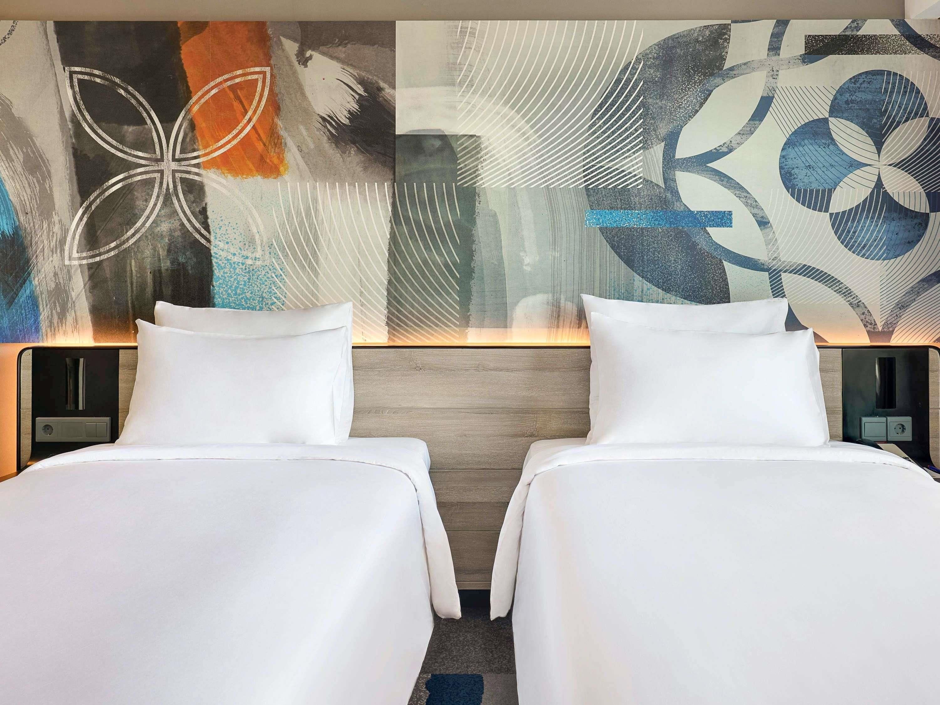 Una habitación de hotel con dos camas, un cuadro abstracto moderno en la pared y un cabecero de madera.