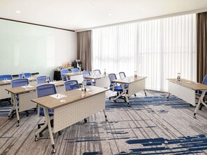 Una sala de conferencias con mesas, sillas, una pizarra y un ventanal con cortinas.