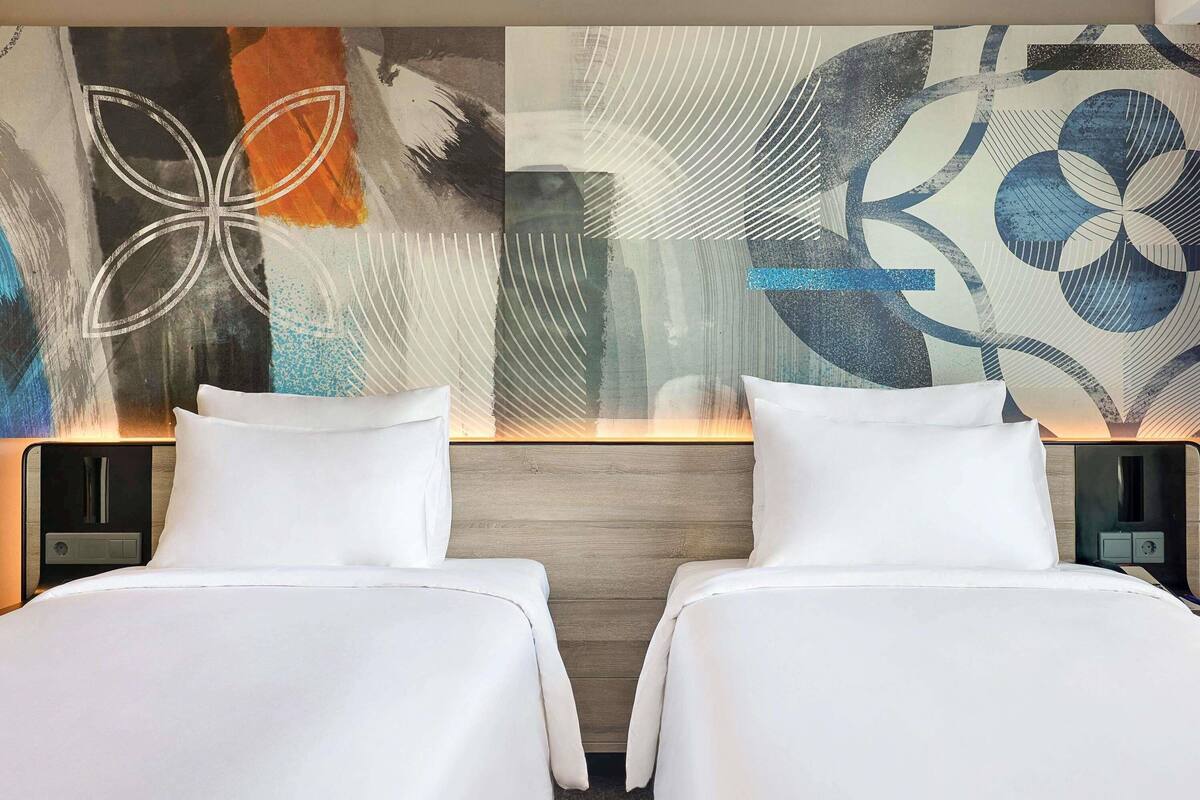 Ein Hotelzimmer mit zwei Betten, einem modernen, abstrakten Wandbild und einem hölzernen Kopfteil.