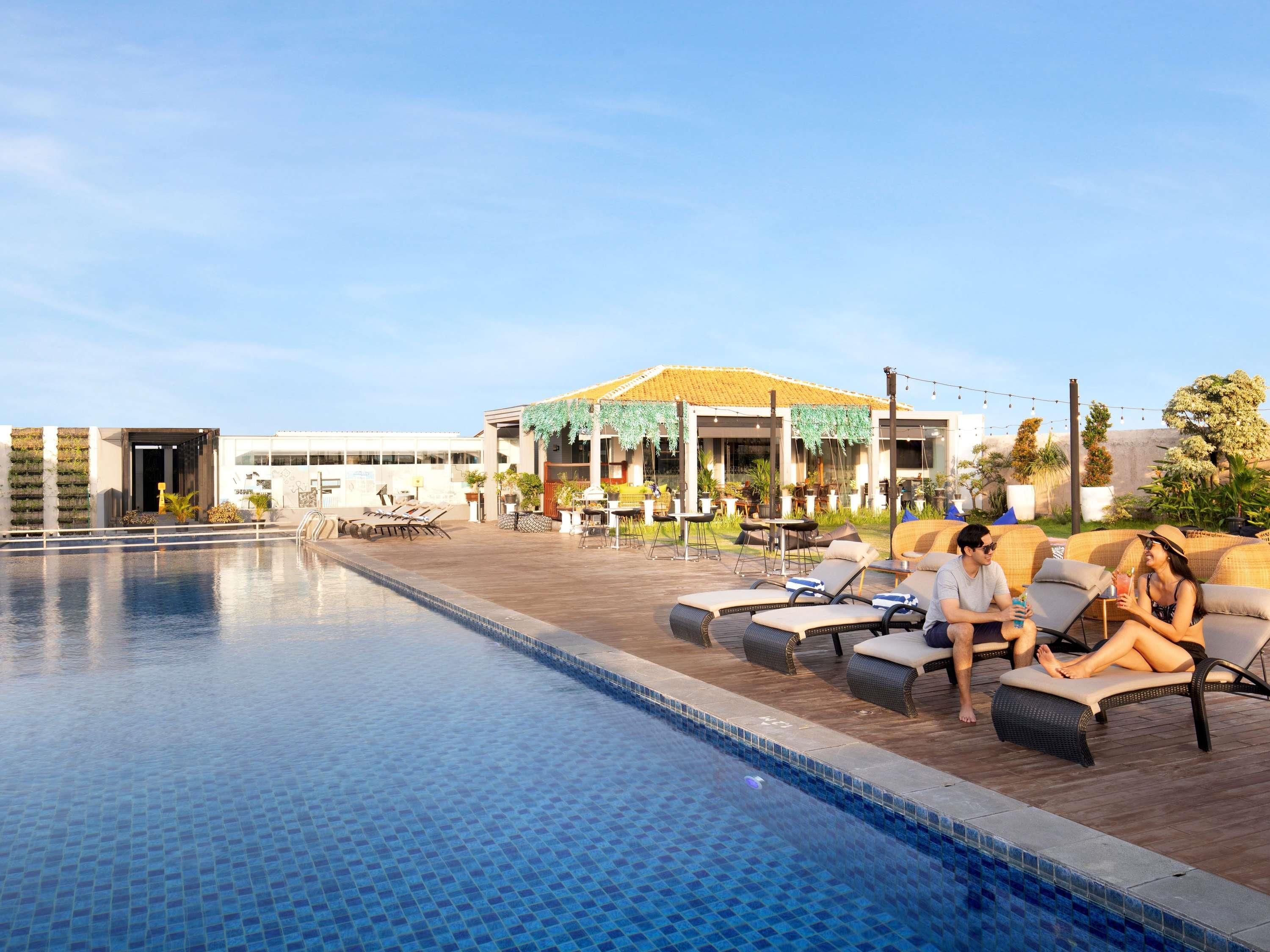 A swimming pool with lounge chairs, a covered seating area, and a building with a yellow roof.
