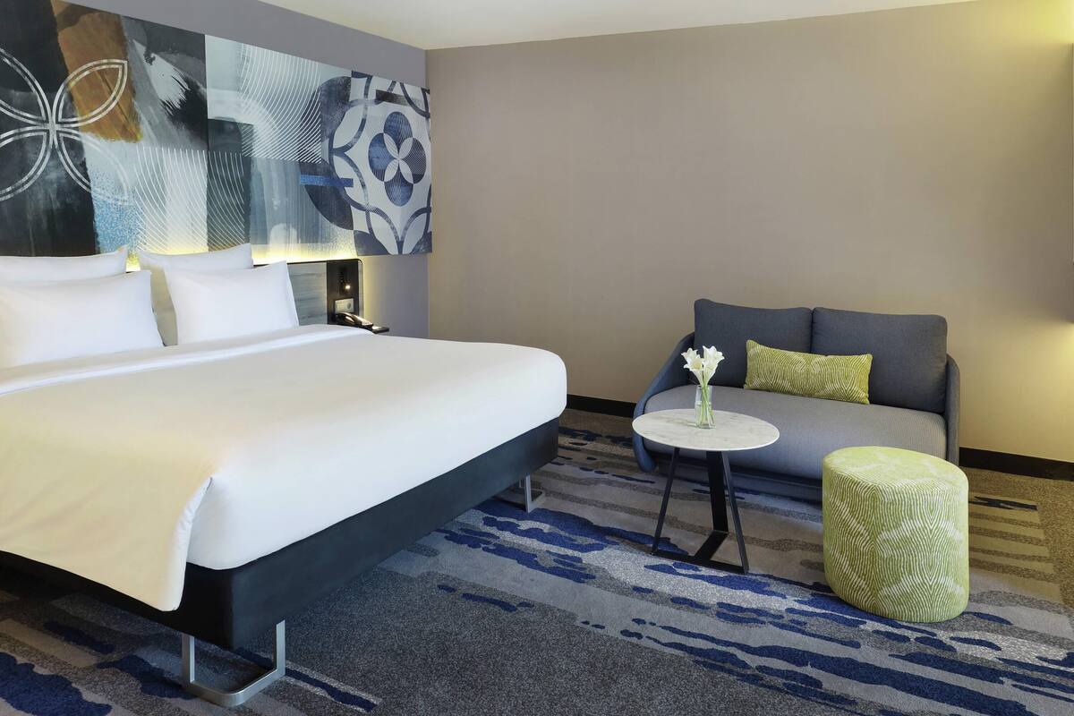 Ein Hotelzimmer mit einem großen Bett, einer Couch, einem kleinen runden Tisch mit einer Vase und einem gemusterten Teppich.