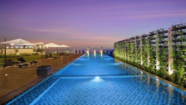 Ein Swimmingpool mit Liegestühlen und Sonnenschirmen, umgeben von Grünflächen und einem Sonnenuntergangshimmel.