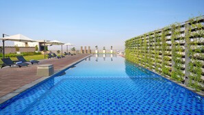 Ein Swimmingpool mit blauen Mosaikfliesen, Liegestühlen, Sonnenschirmen und einer Wand mit vertikalen Gärten.