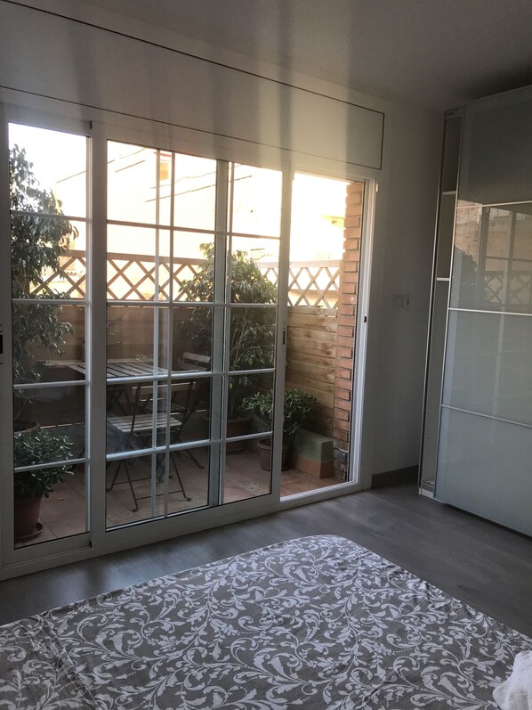A room with a sliding glass door leading to a patio area with a table and chairs, a potted plant, and a brick wall. - Kamelly Guest House (Badalona)