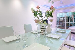 Un comedor moderno con una mesa de vidrio, sillas blancas y un jarrón de rosas rosadas.