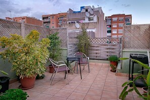 Terraza en la azotea con plantas en macetas, una mesa y sillas.