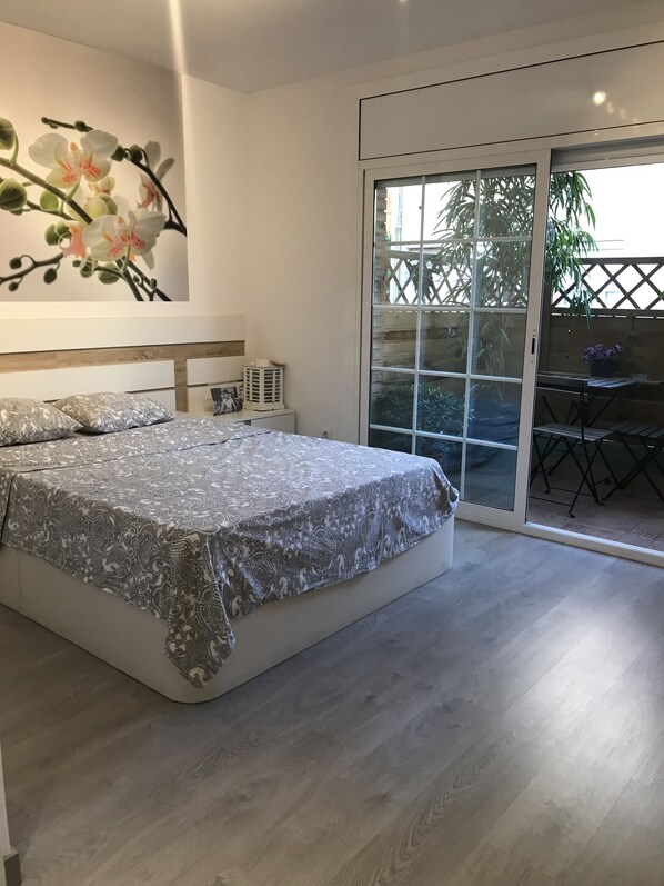 Un dormitorio con una cama grande, una mesita de noche, una obra de arte colgada en la pared y un ventanal corredero que da a un espacio al aire libre.