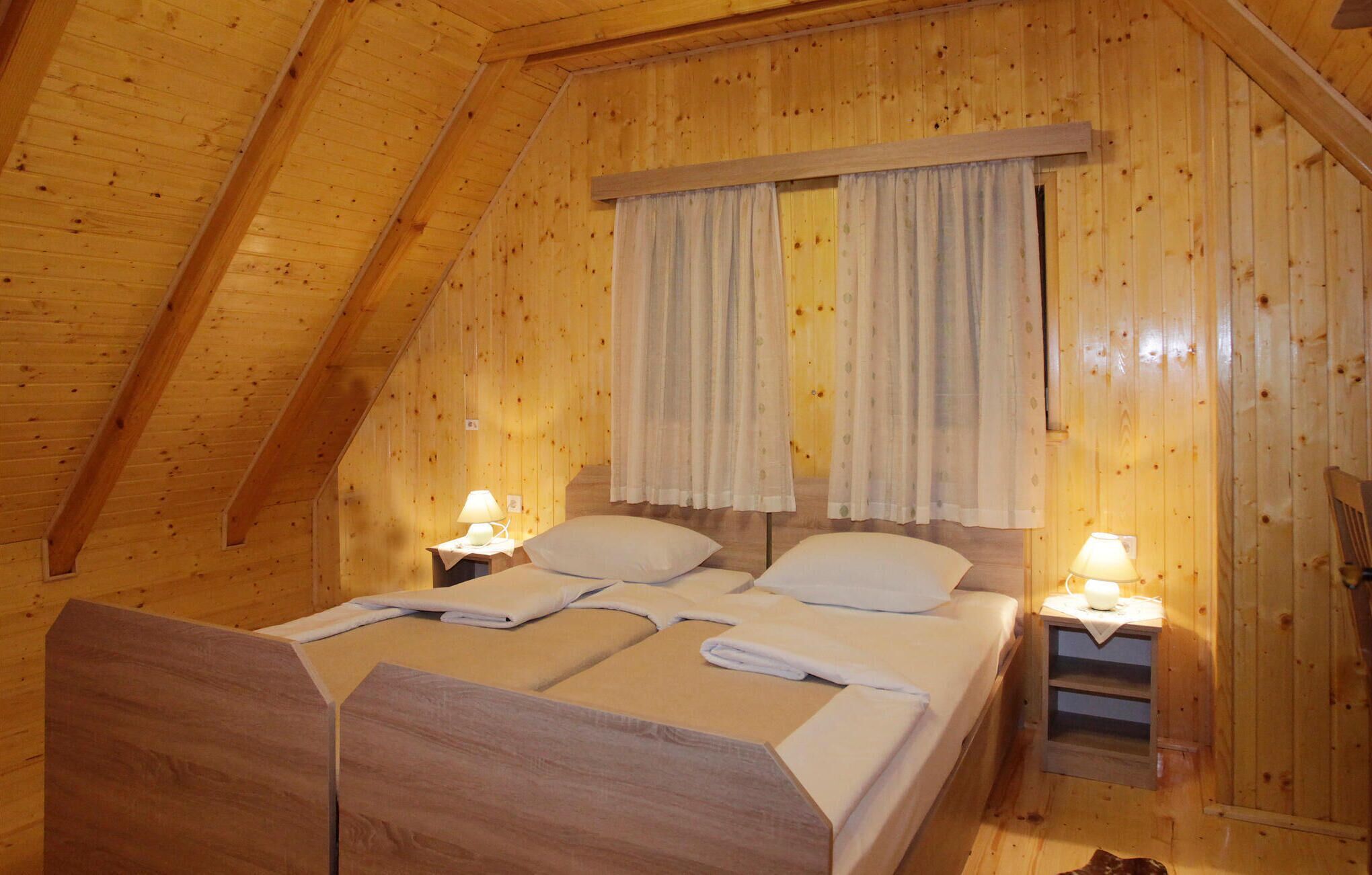 A cozy wooden room with a bed, two bedside tables, and a window with curtains.