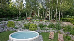 A hot tub surrounded by a stone wall, two wooden chairs, and a garden with various plants and trees. - 4 bedroom gorgeous home in Breze (Breze)