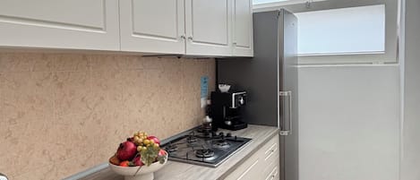 A kitchen with a gas stove, a sink, cabinets, a bowl of fruit, and a refrigerator.