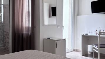 Habitación de hotel con cama, escritorio, silla, televisor, armario y espejo.