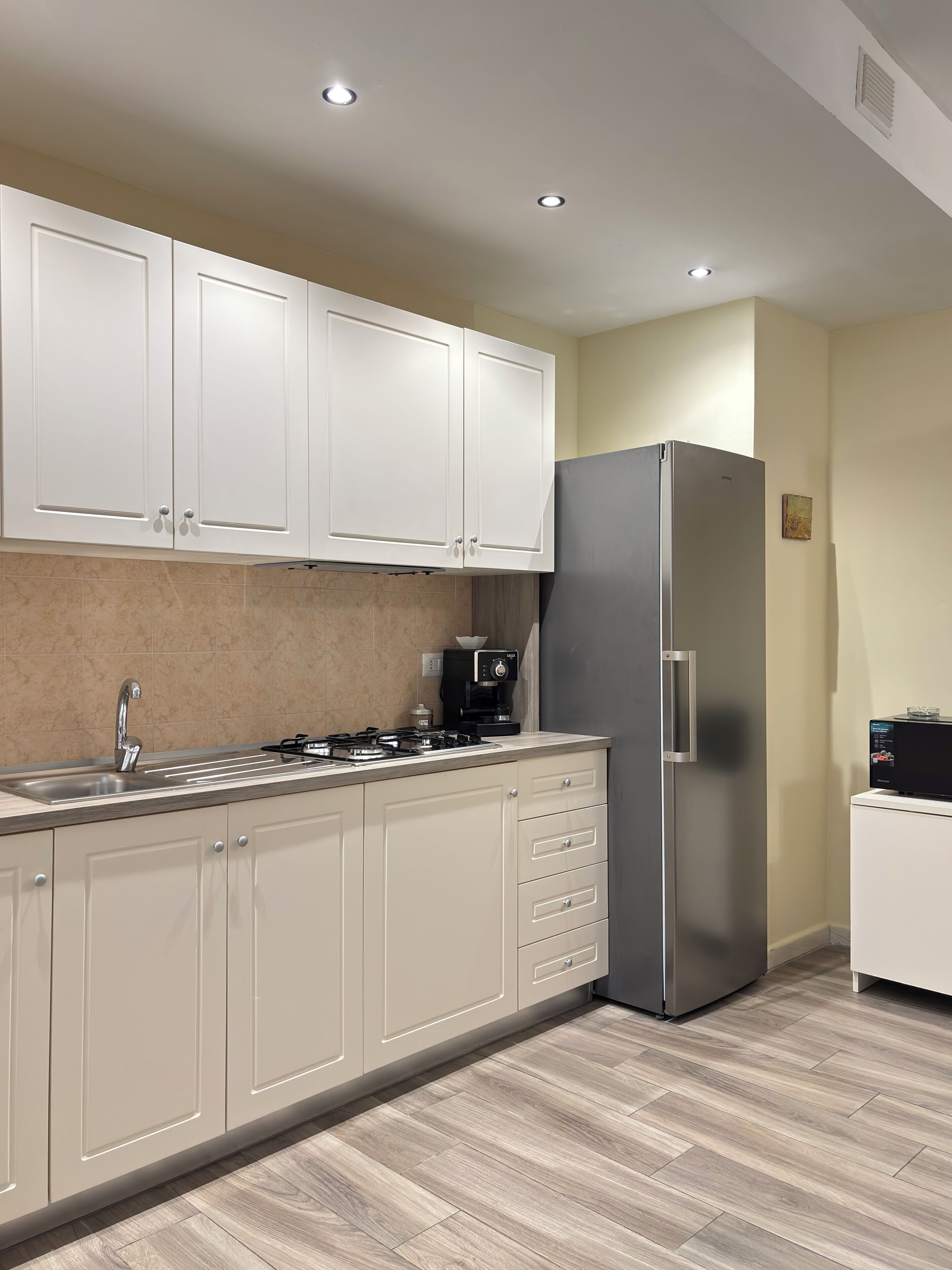 A kitchen with white cabinets, a stainless steel refrigerator, a coffee maker, and a sink.