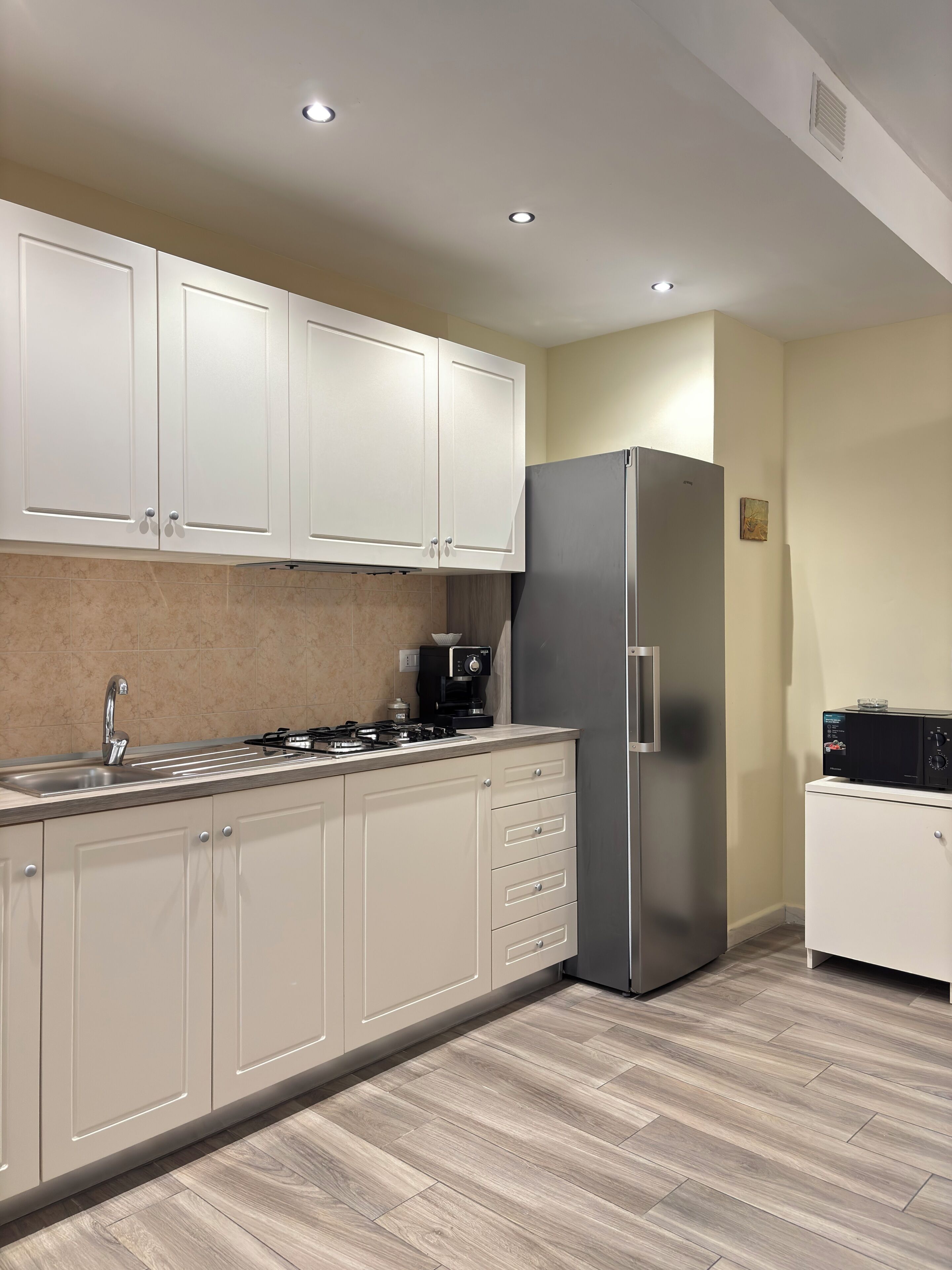 A modern kitchen with white cabinets, a stainless steel refrigerator, a coffee maker, and a microwave.