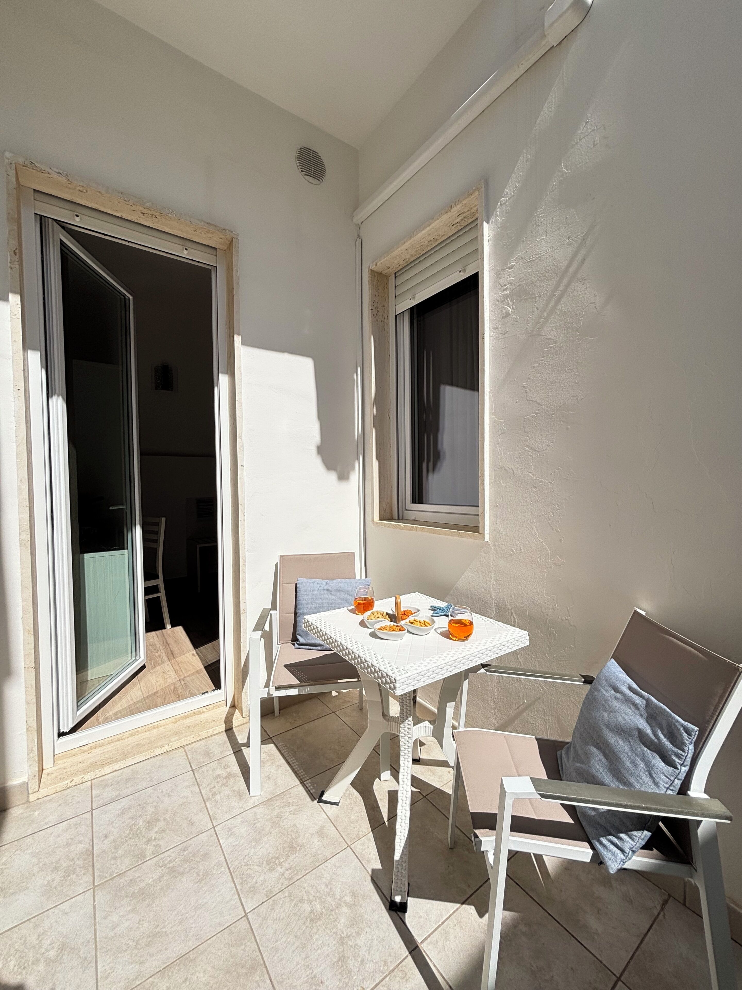 A balcony with a table set for two, chairs, and a sliding glass door leading to an interior space.