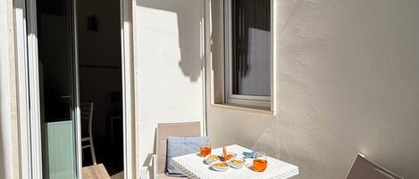 A balcony with a table set for two, chairs, and a sliding glass door leading to an interior space.