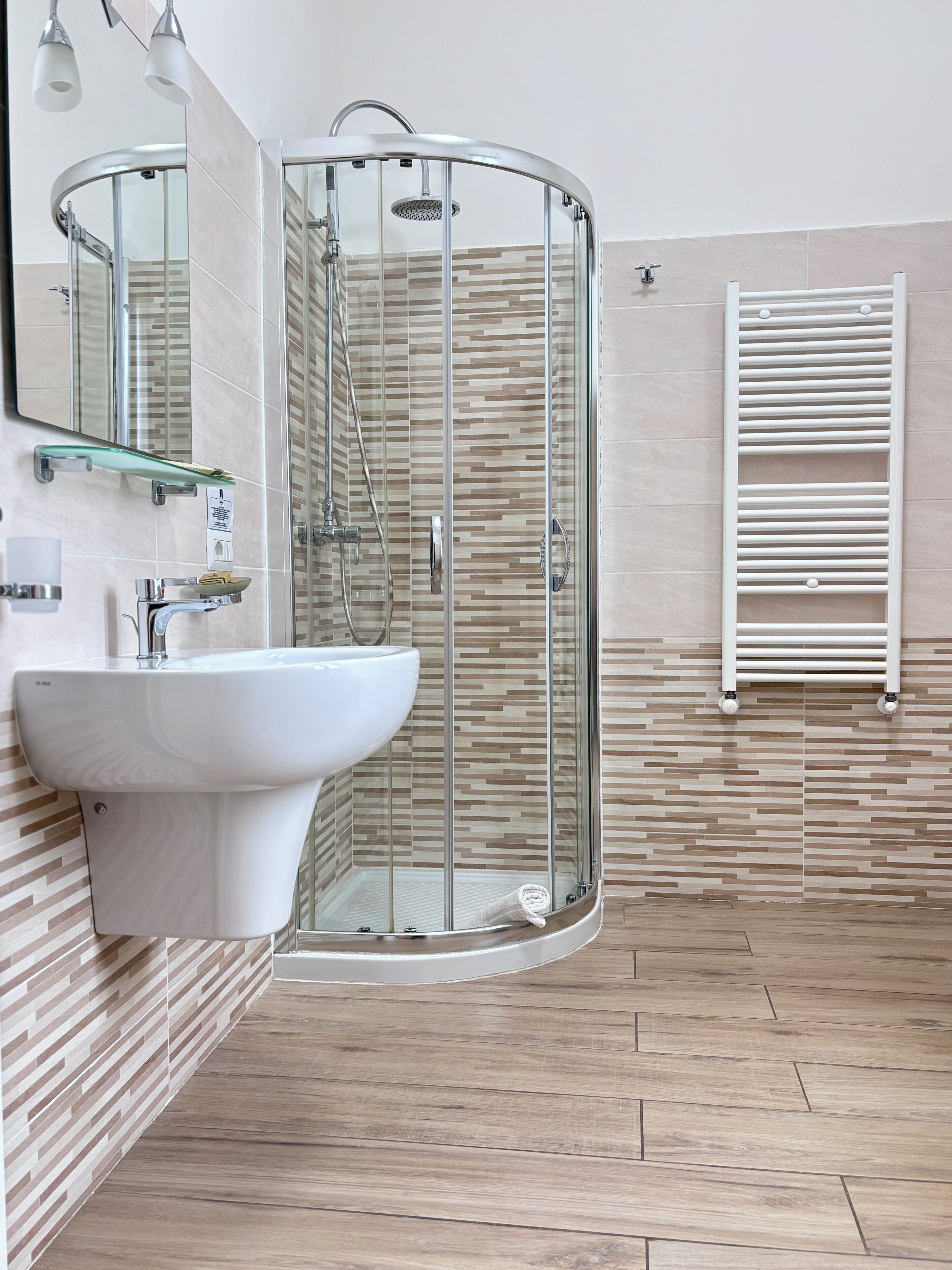 Un baño moderno con cabina de ducha de vidrio curvo, un lavabo blanco y un perchero para toallas.