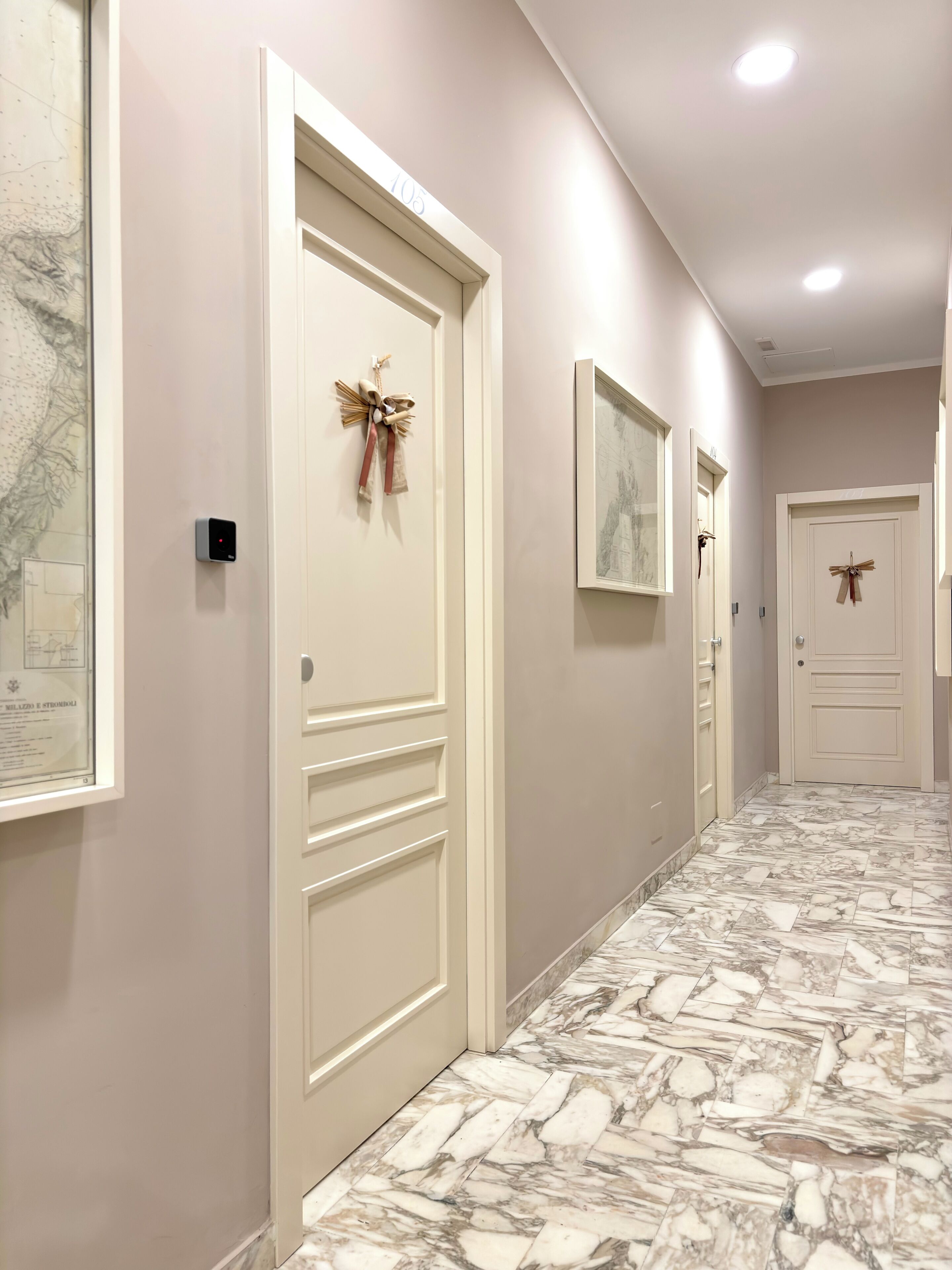 A hallway with white doors, a marble floor, and framed artwork on the walls.