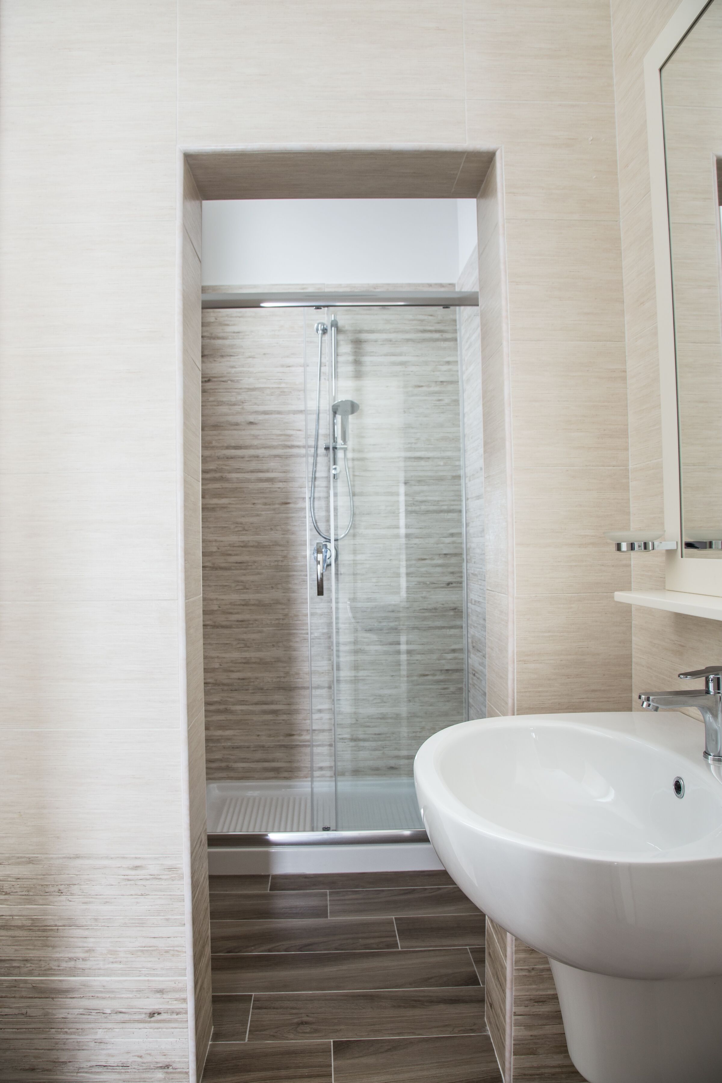 A modern bathroom with a glass-enclosed shower, a white sink, and a mirror above it.