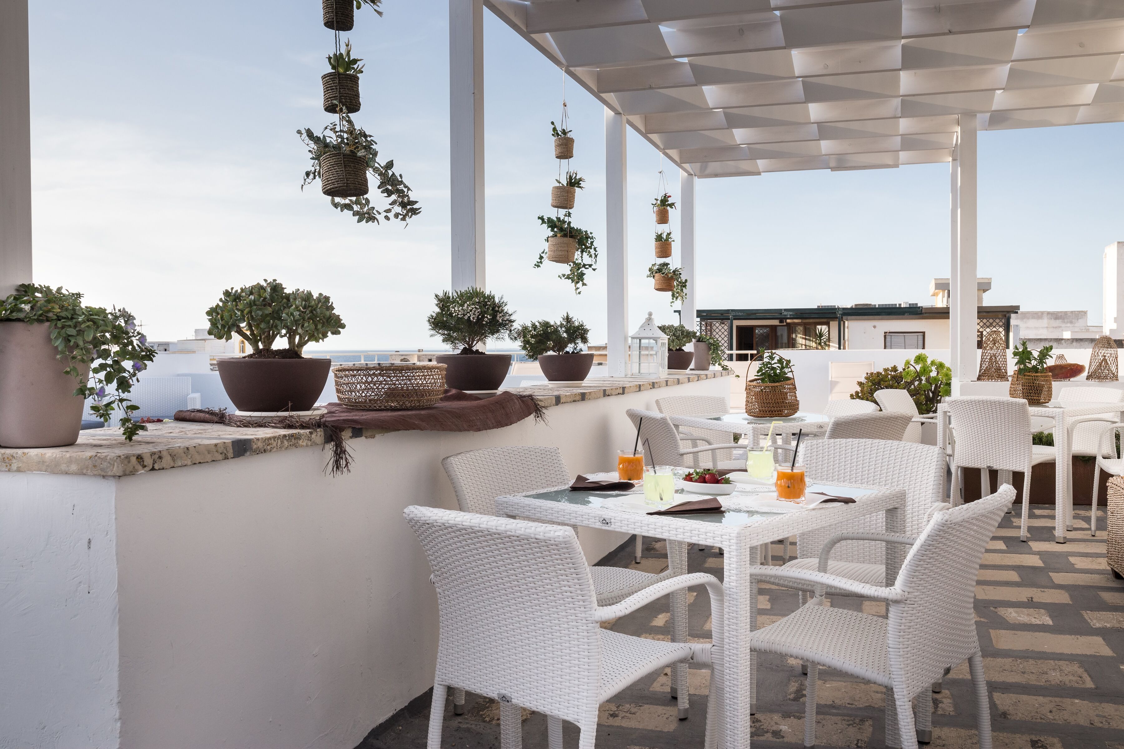 A rooftop terrace with white wicker furniture, potted plants, and a view of the cityscape.