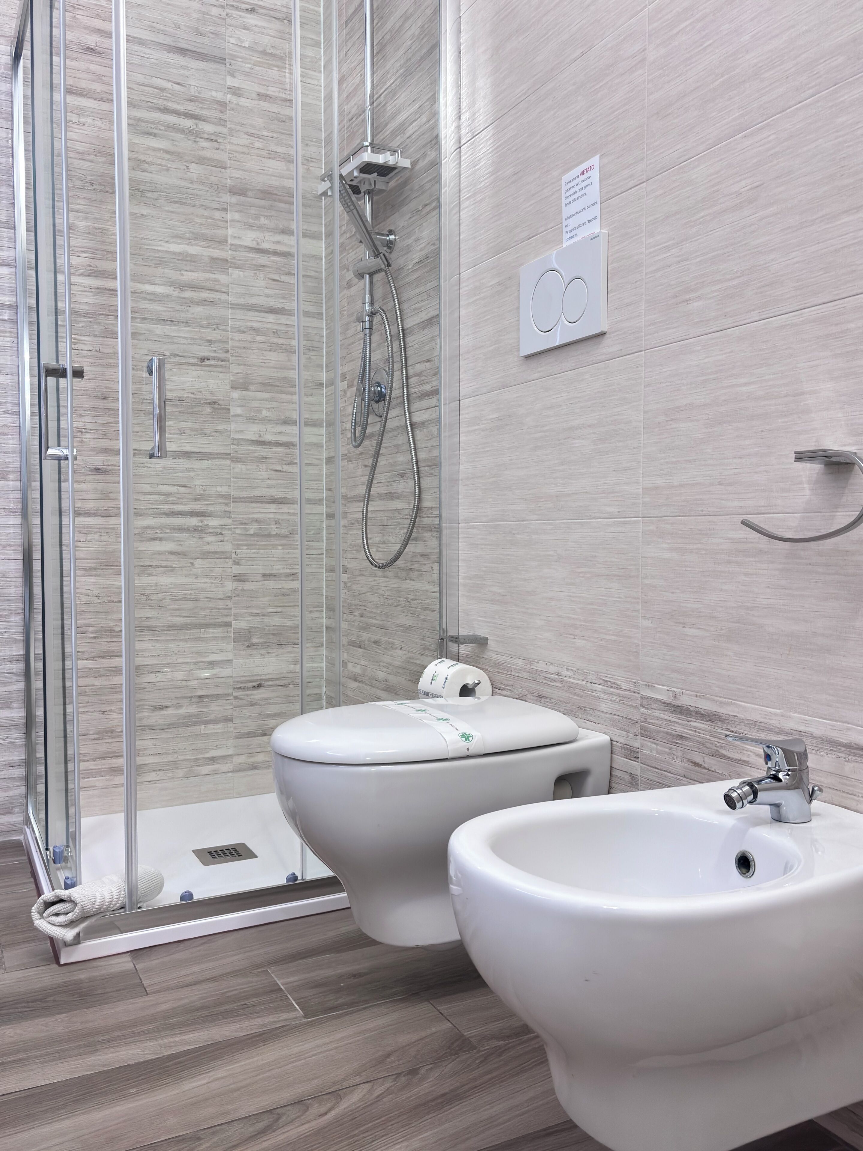 Un bany modern amb dutxa de vidre, dues vàteres i un bidet.