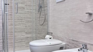 Un bany modern amb dutxa de vidre, dues vàteres i un bidet.
