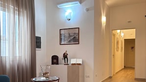 A modern living room with a wooden floor, a sofa, a table with a glass top, a wall-mounted air conditioner, a framed picture, and a door leading to another room. - Faro Bianco Gallipoli (Gallipoli)