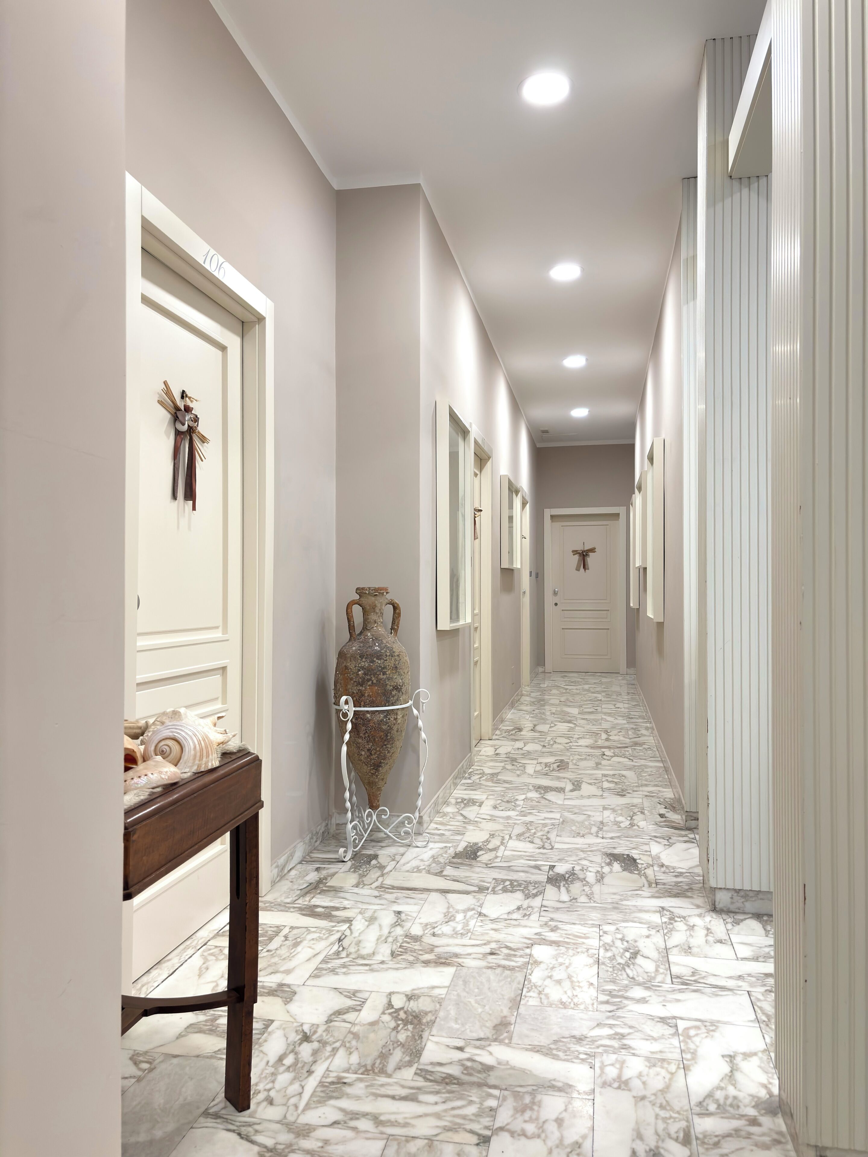 A hallway with marble flooring, white walls, and doors with numbers.