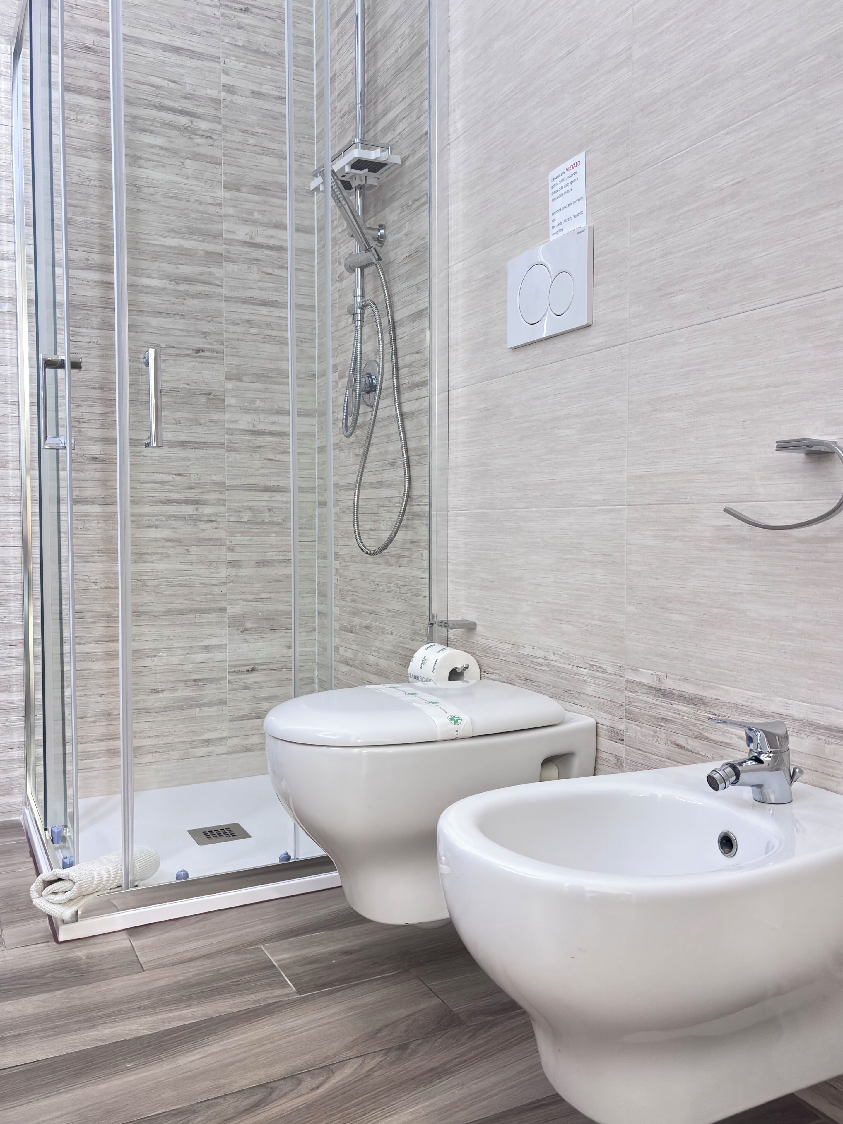 A modern bathroom with a glass shower enclosure, two toilets, and two sinks.