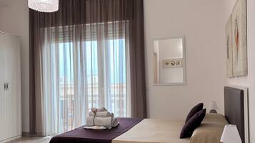 A hotel room with a bed, bedside table, lamp, air conditioning unit, and a view of the outdoors.