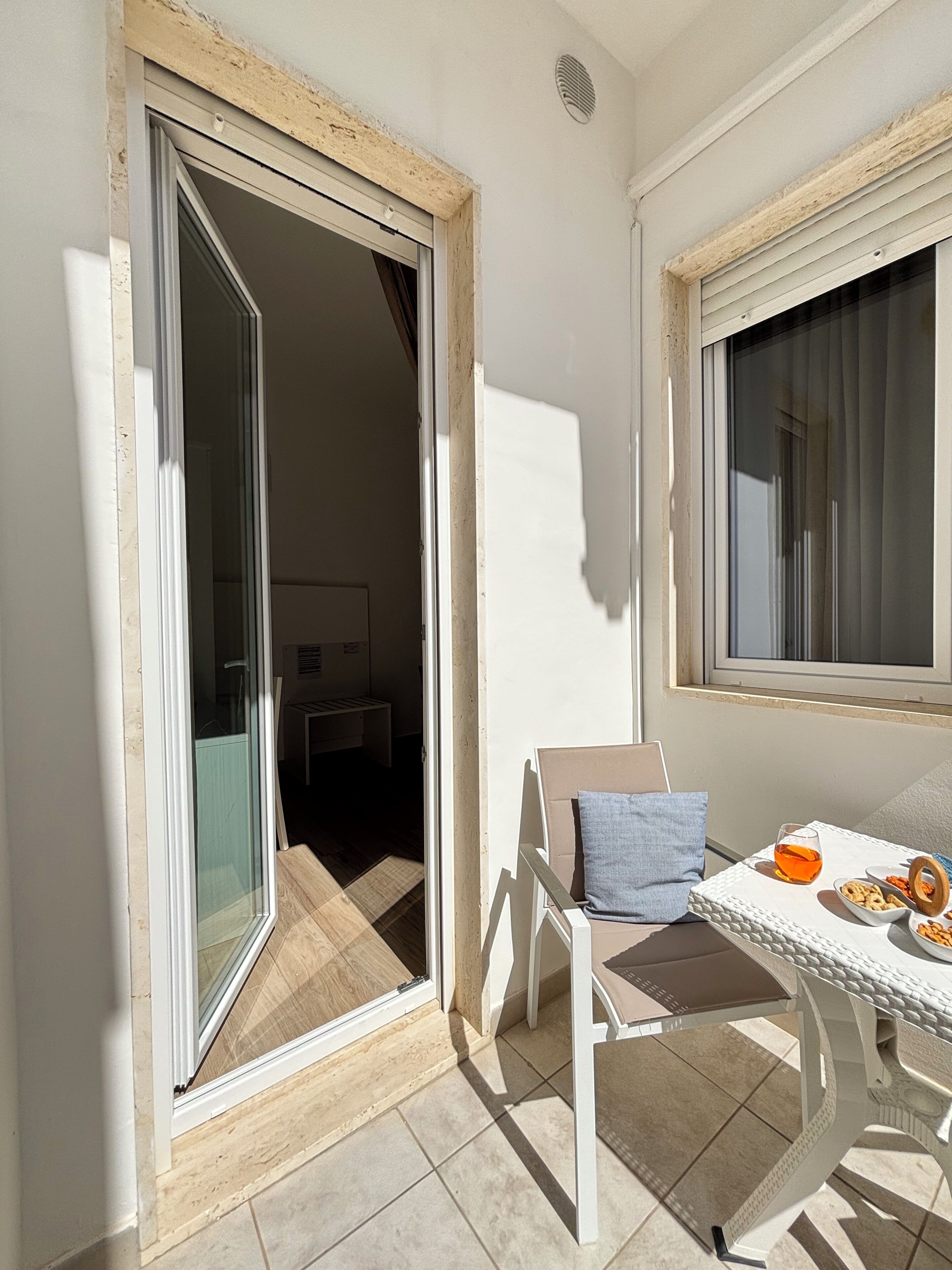 A balcony with a table set with snacks, a chair, and a window with curtains.