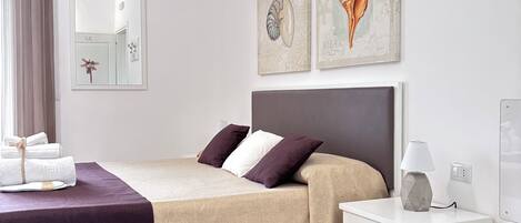 A modern hotel room with a bed, bedside table, lamp, and artwork on the wall.