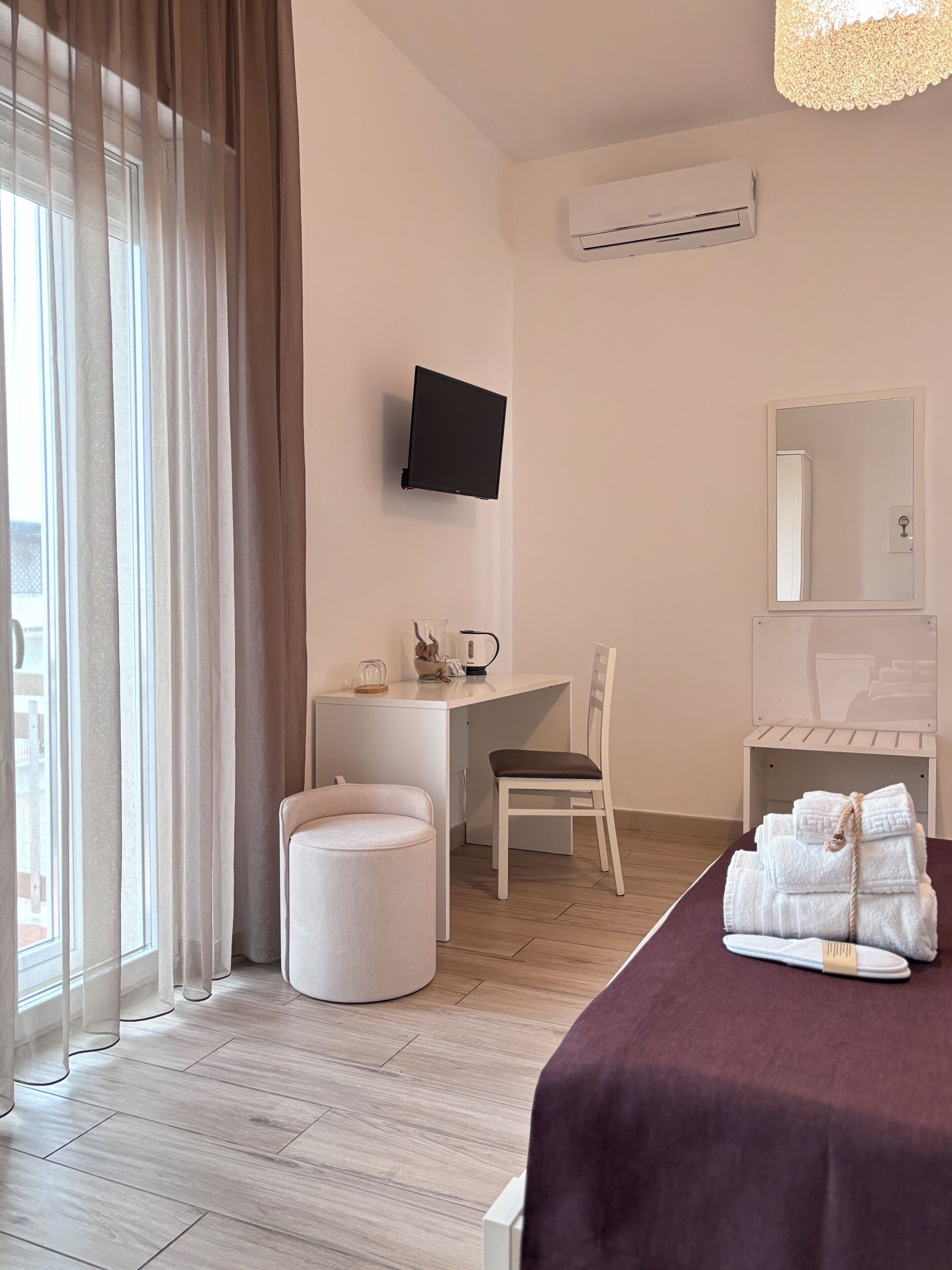 Habitación de hotel con cama, escritorio, silla, televisor y aire acondicionado.