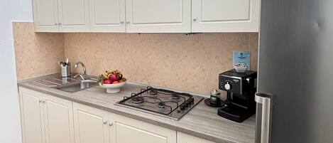 A modern kitchen with white cabinets, a stainless steel refrigerator, a gas stove, and a coffee machine.