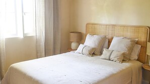A large bed with white linens, a woven headboard, and a bedside table with a lamp. - Vumba - House of the Lizard (Arganil)