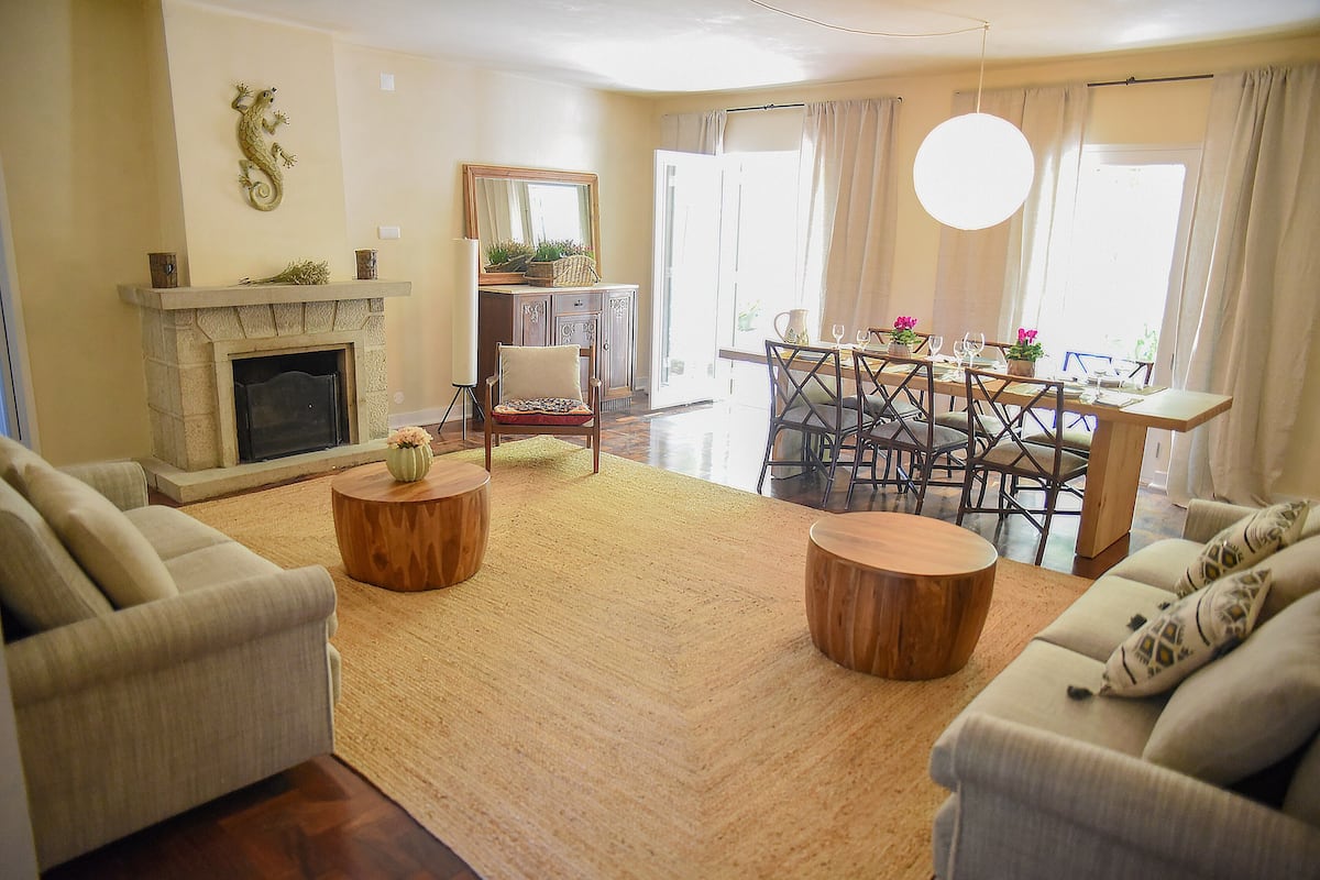 A living room with a fireplace, sofas, a dining area with a table and chairs, and a large window with curtains.