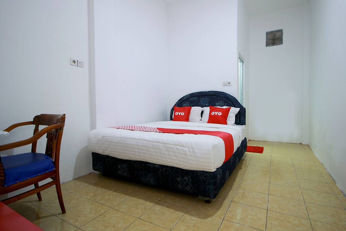 A small, clean room with a single bed, a wooden chair, and a small table.