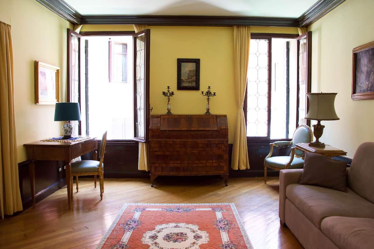 Una habitación con escritorio de madera, una silla, un sofá y un tapete estampado.