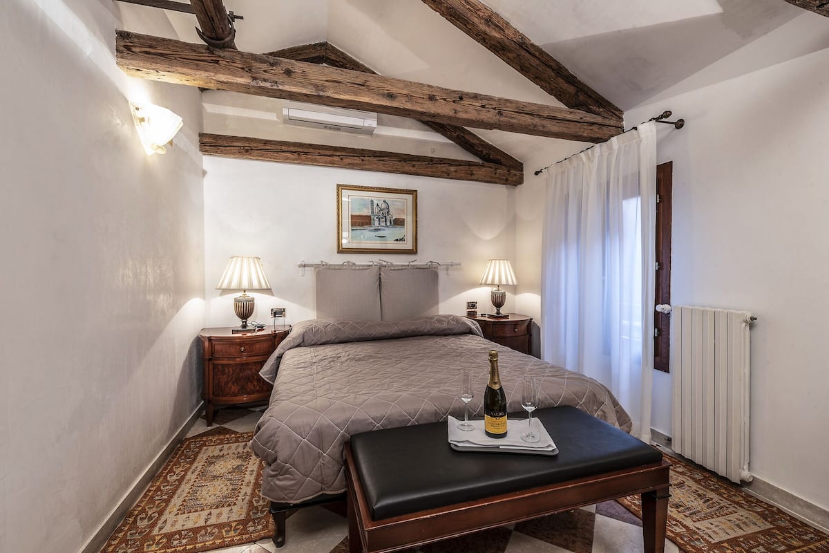 Un dormitorio con una cama, lámparas de noche, una botella de champán y una bandeja con vasos.