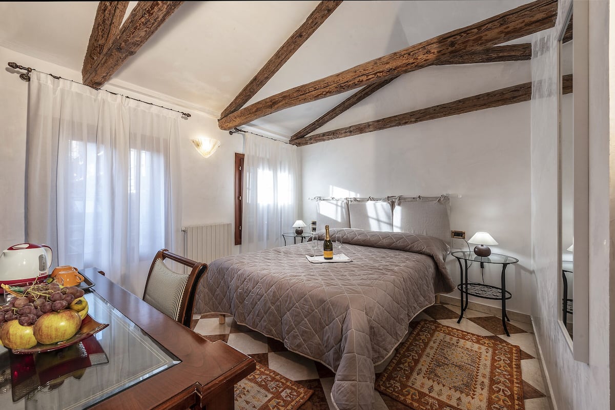 Un dormitorio con cama, mesitas de noche, una mesa con fruta y vistas al exterior.