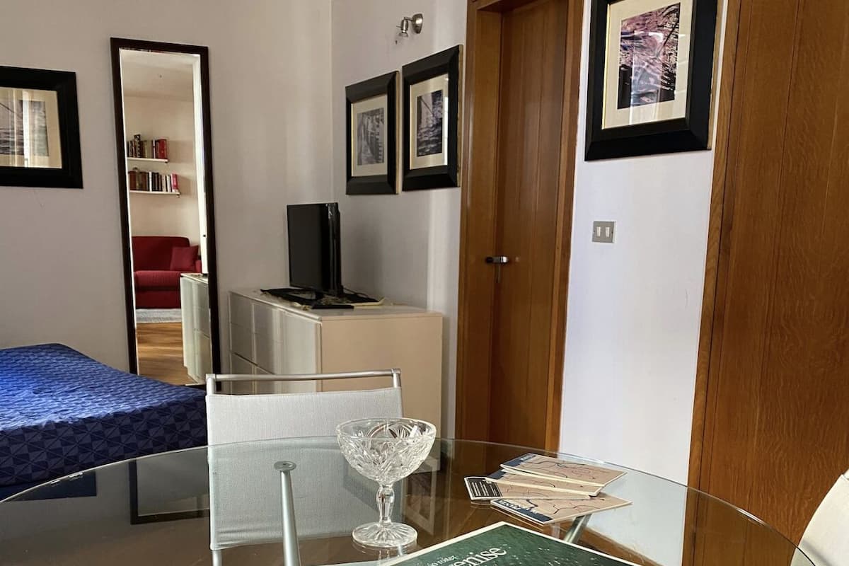 Una habitación pequeña con una mesa de vidrio, una cama, un escritorio y un armario.