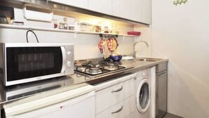 A compact kitchen with a microwave, stove, and washing machine. - Anzolo Palace (Venice)